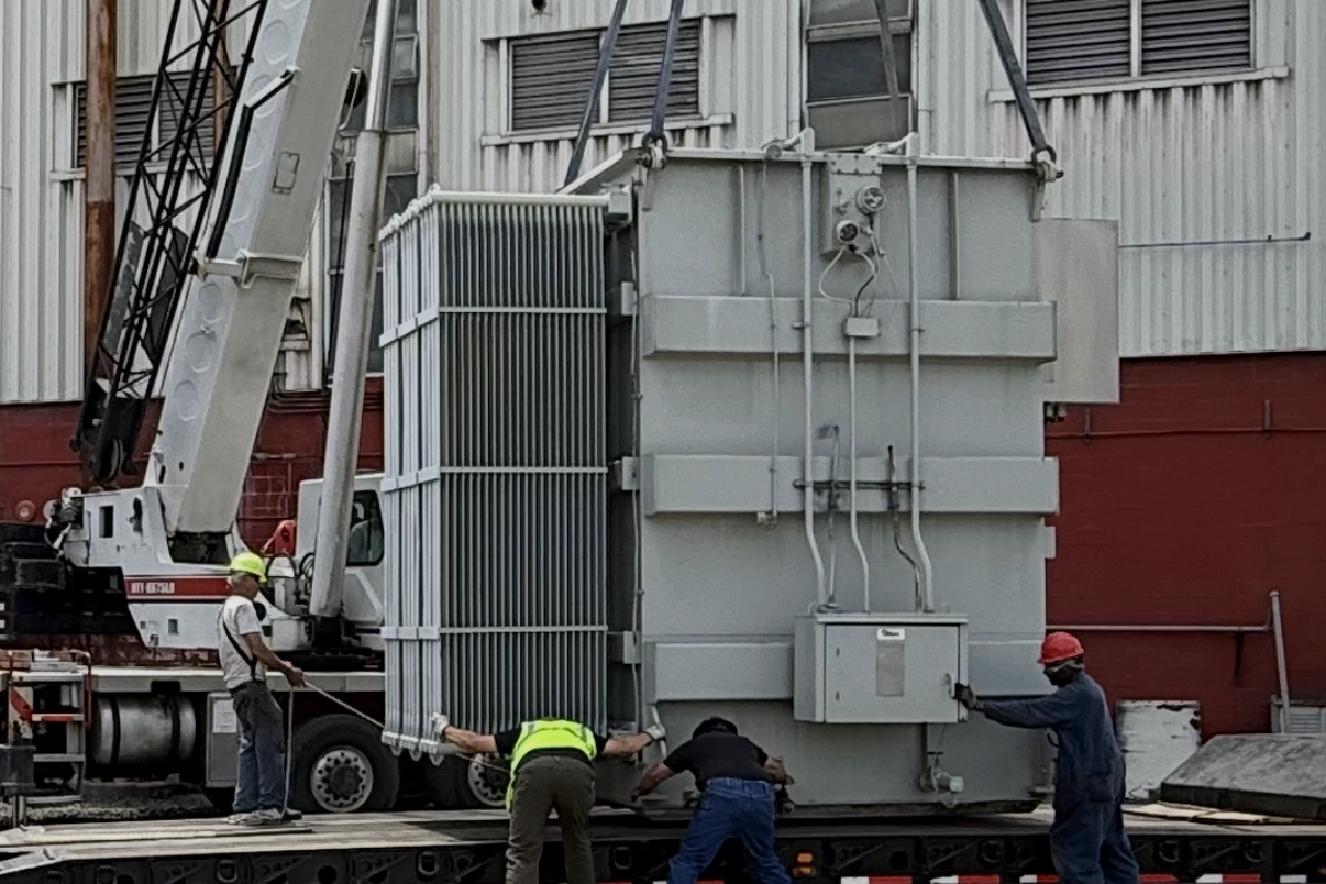 Crane lifting a power transformer onto a lowboy trailer while the removal crew guides the load — New York, NY