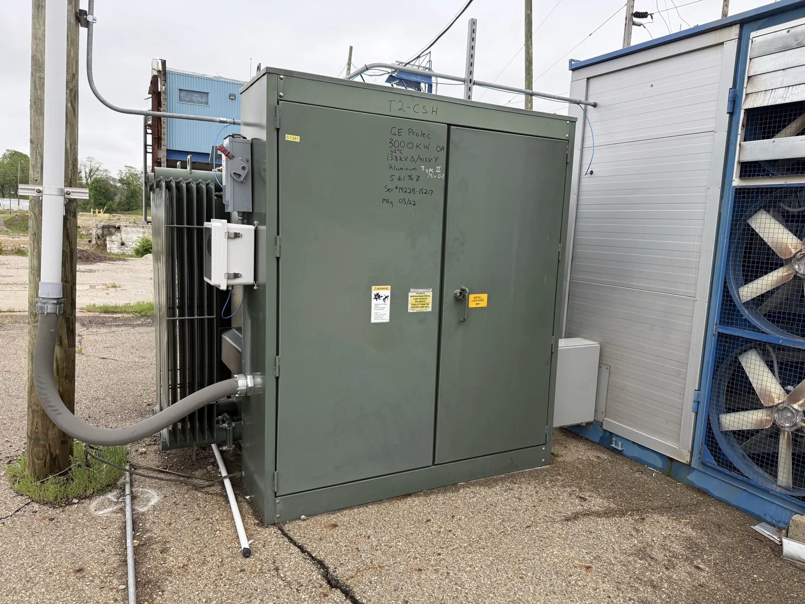 Green pad-mount transformer with radiator fins beside a plant building — Springfield, MA